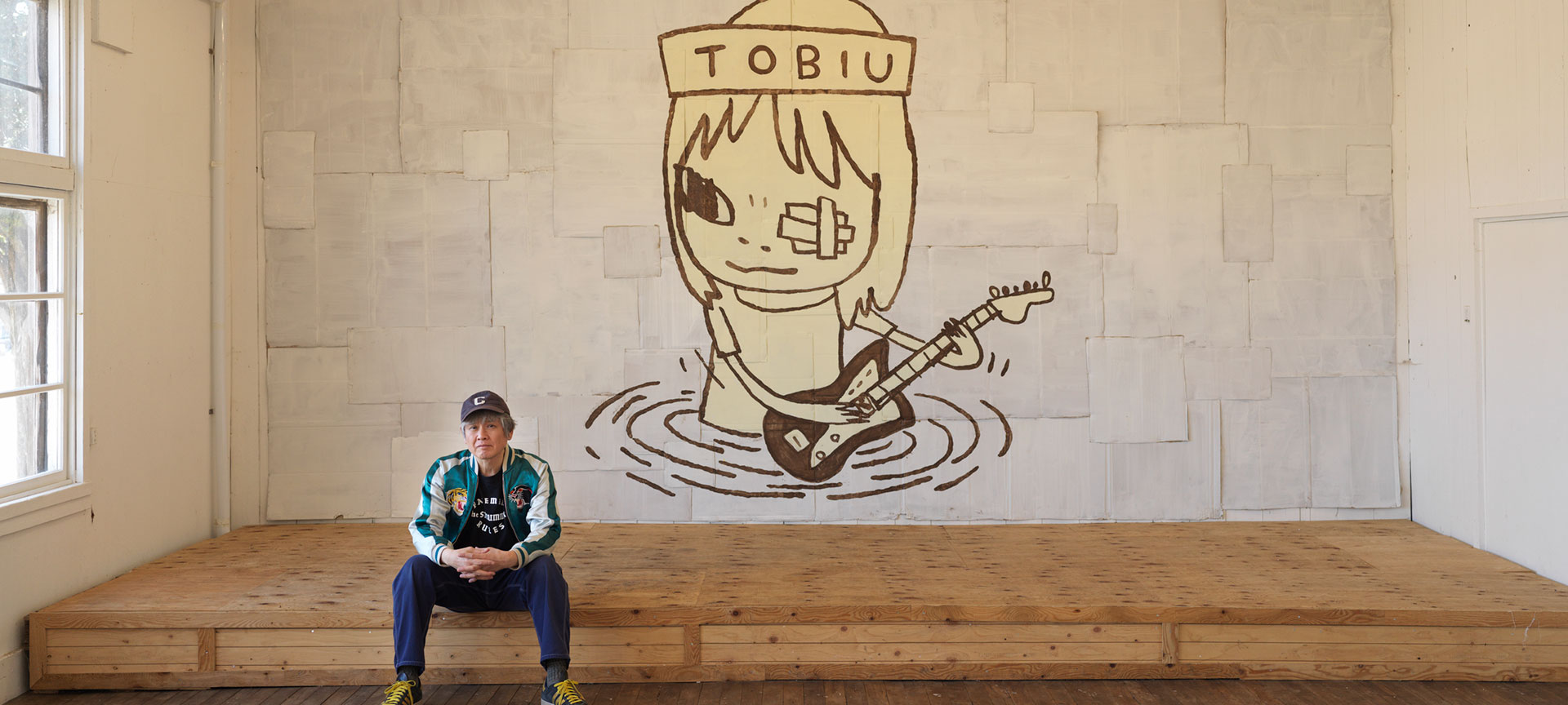 Yoshitomo Nara seated before TOBIU, 2019. Artist